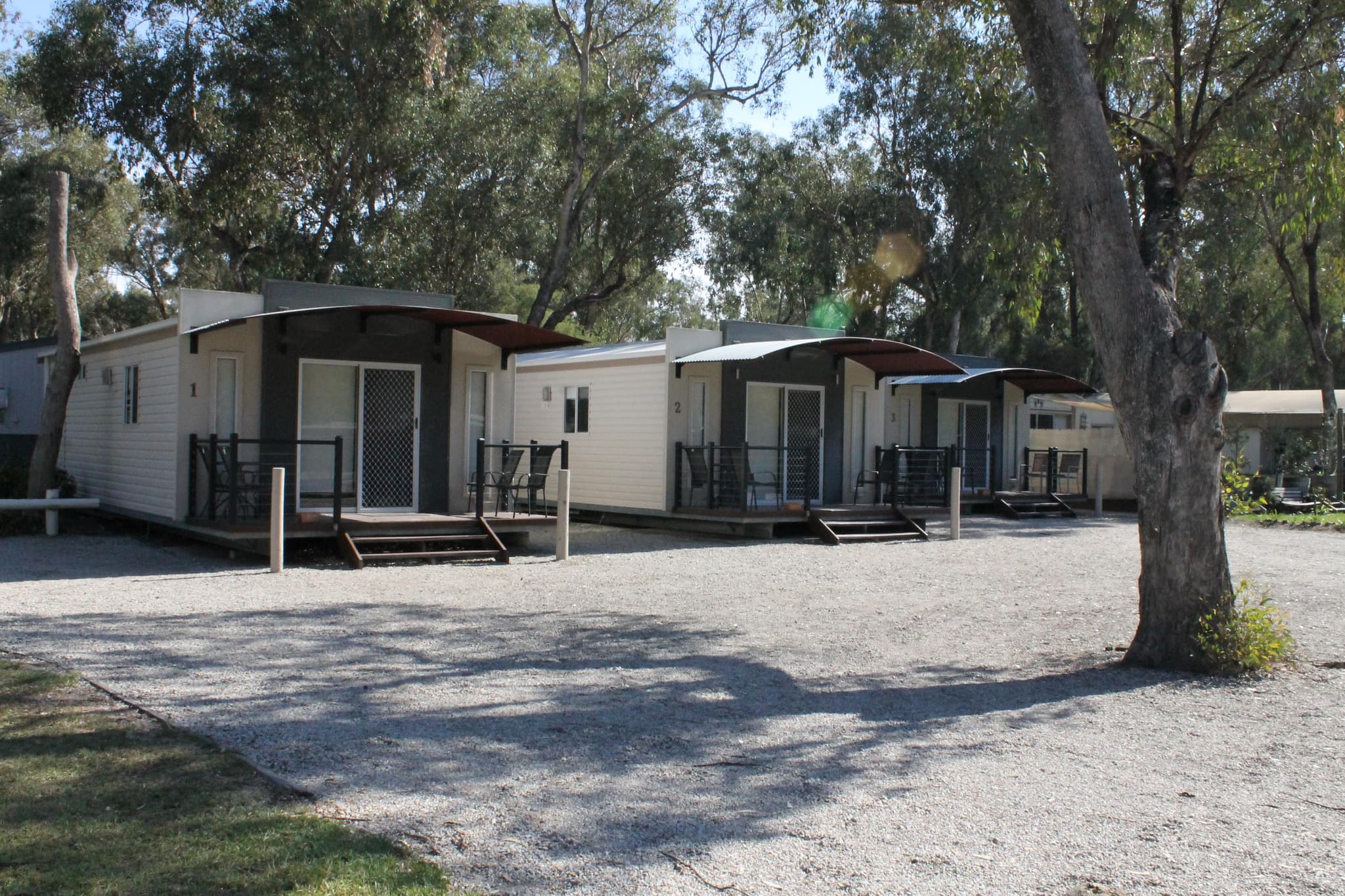 Cream cabins numbered 1 to 3 with dark curved awnings and timber decks at Torrumbarry Weir Holiday Park, Patho VIC