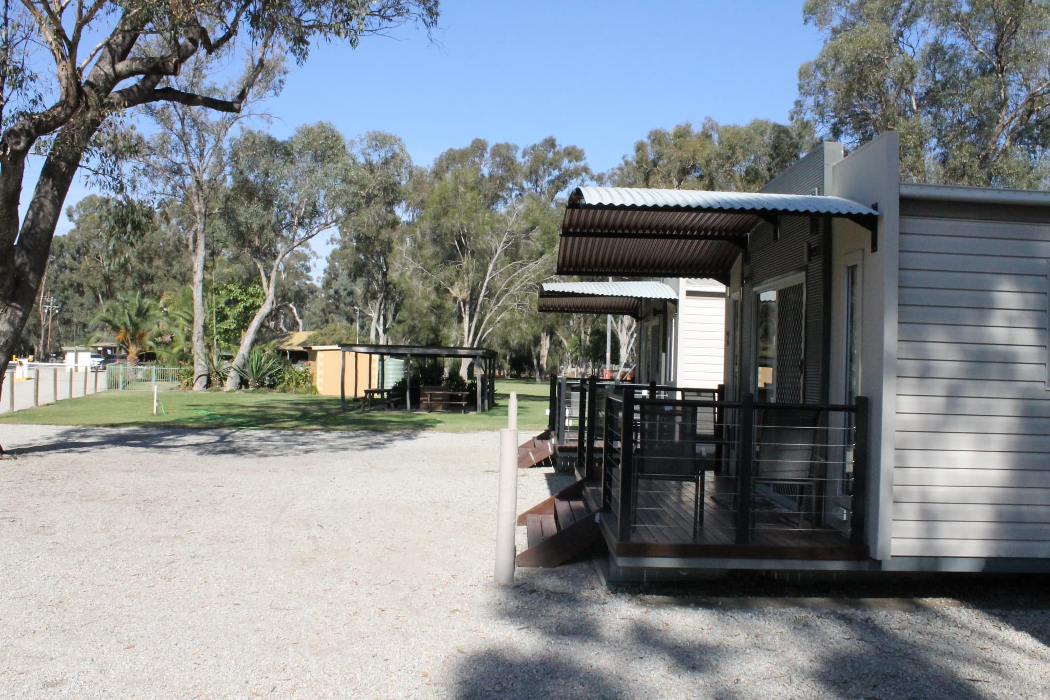 Fleetwood Rainbow Cabin timber deck with curved awning at Torrumbarry Weir Holiday Park, gum trees and lawn behind