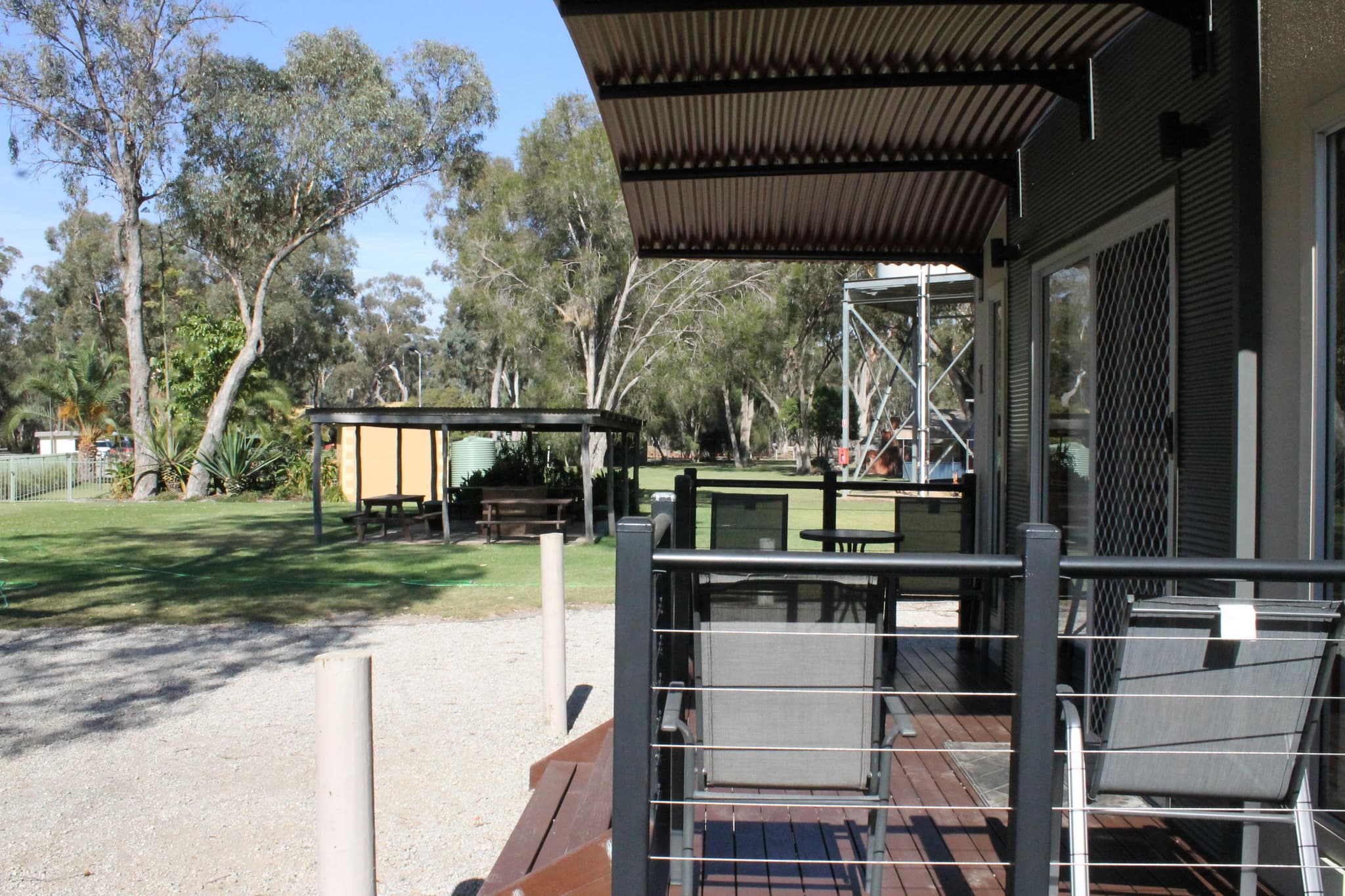 Timber deck with outdoor chairs at Fleetwood Rainbow Cabin, Torrumbarry Weir Holiday Park, overlooking shaded lawn and picnic tables among gum trees