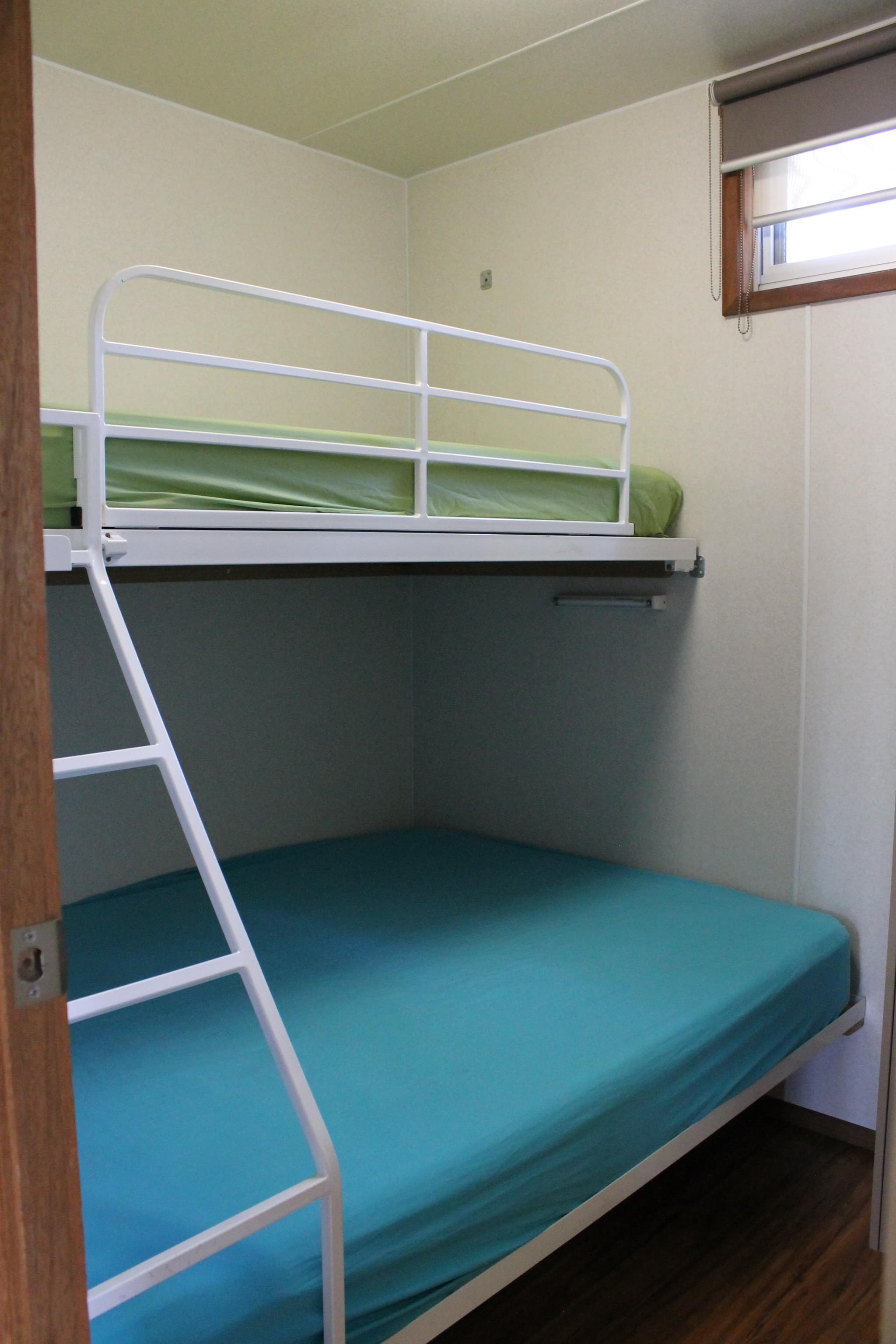 Bunk beds with teal and green linen inside a Fleetwood Rainbow Cabin bedroom at Torrumbarry Weir Holiday Park, Patho VIC