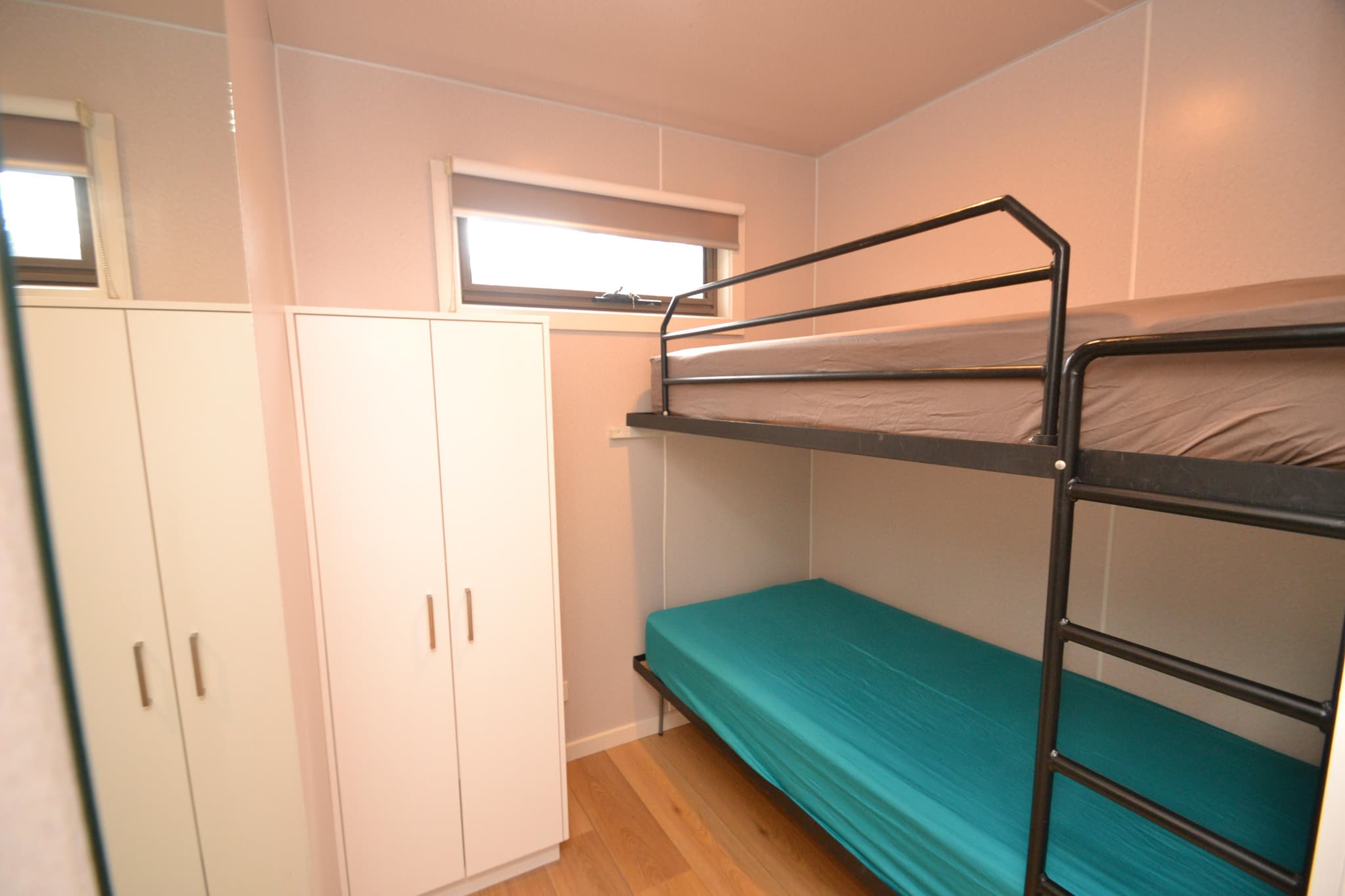 Bunk bed bedroom with black metal frame, teal and grey linen, white wardrobes and timber flooring in a Deluxe Riverview Cabin at Torrumbarry Weir Holiday Park