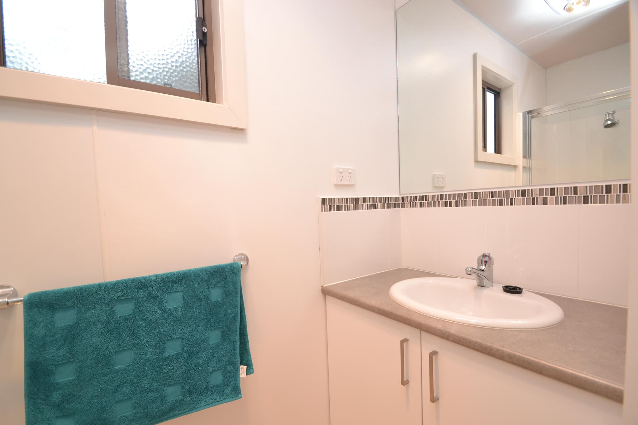 Ensuite bathroom in a Deluxe Riverview Cabin at Torrumbarry Weir Holiday Park, with white vanity, mosaic tile splashback and teal towel