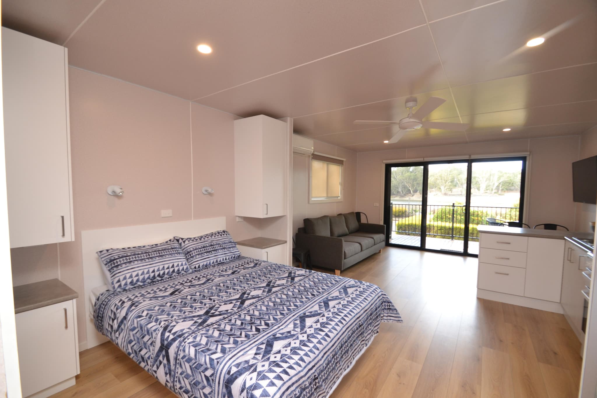 Open-plan cabin at Torrumbarry Weir Holiday Park with queen bed, kitchenette and deck opening onto river views