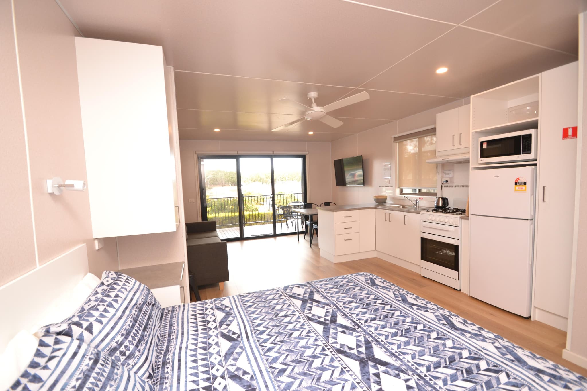 Open-plan deluxe cabin at Torrumbarry Weir Holiday Park with double bed, kitchenette and river-view balcony