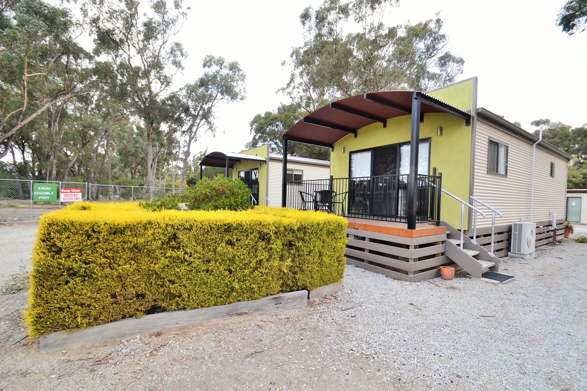 Lime green Deluxe Riverview Cabin exterior with covered timber deck at Torrumbarry Weir Holiday Park, surrounded by gum trees