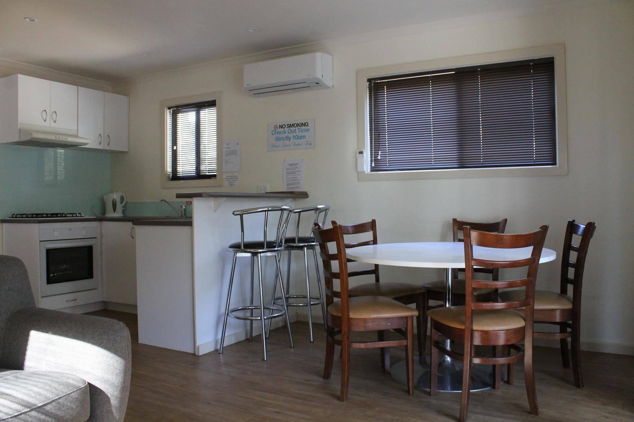 Open-plan kitchen and dining area in the Southern Cross Cabin at Torrumbarry Weir Holiday Park, with round table, four chairs and breakfast bar stools