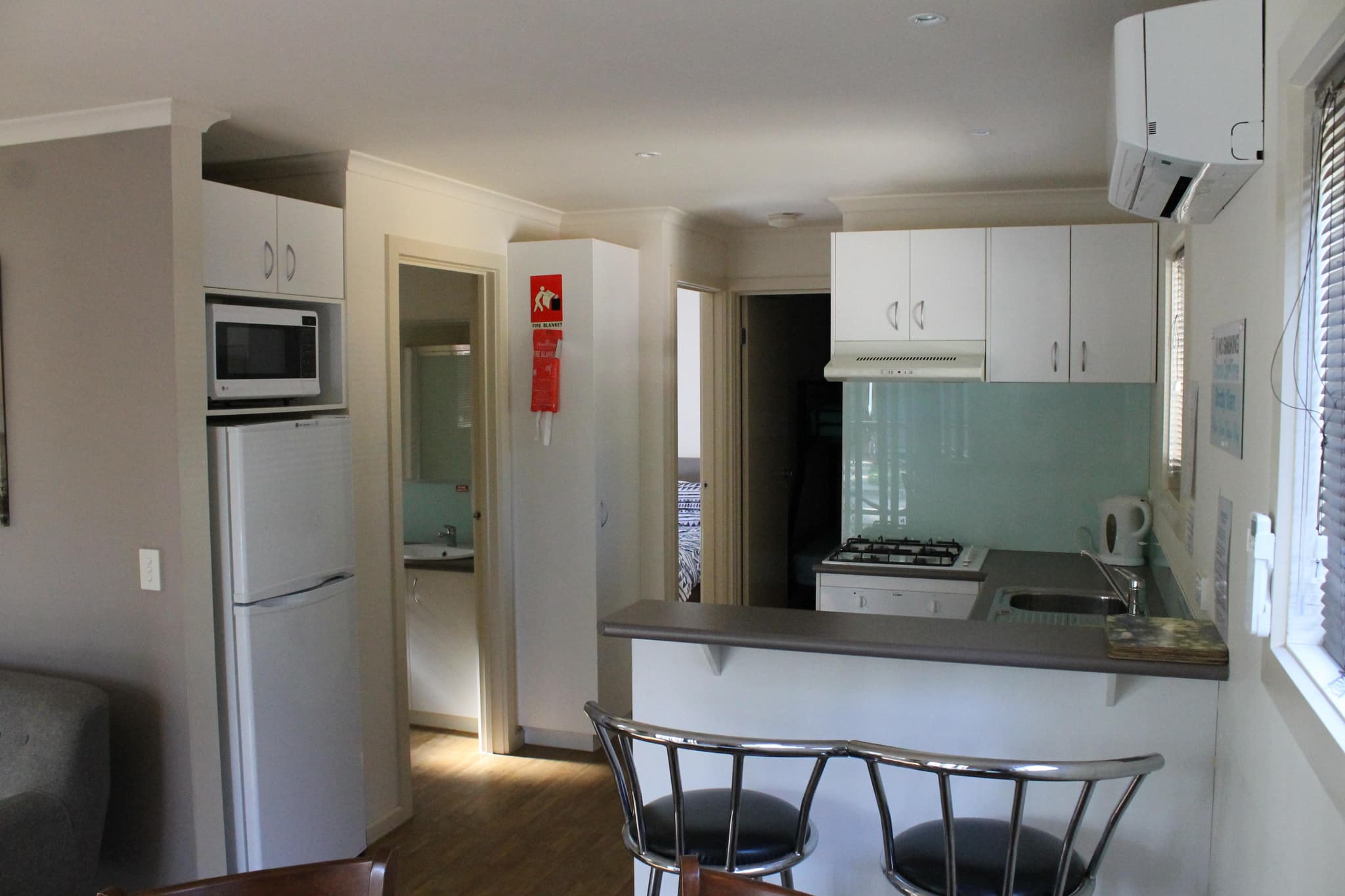 Cabin kitchen with breakfast bar and stools at Torrumbarry Weir Holiday Park, showing fridge, gas cooktop and glimpse of bedroom