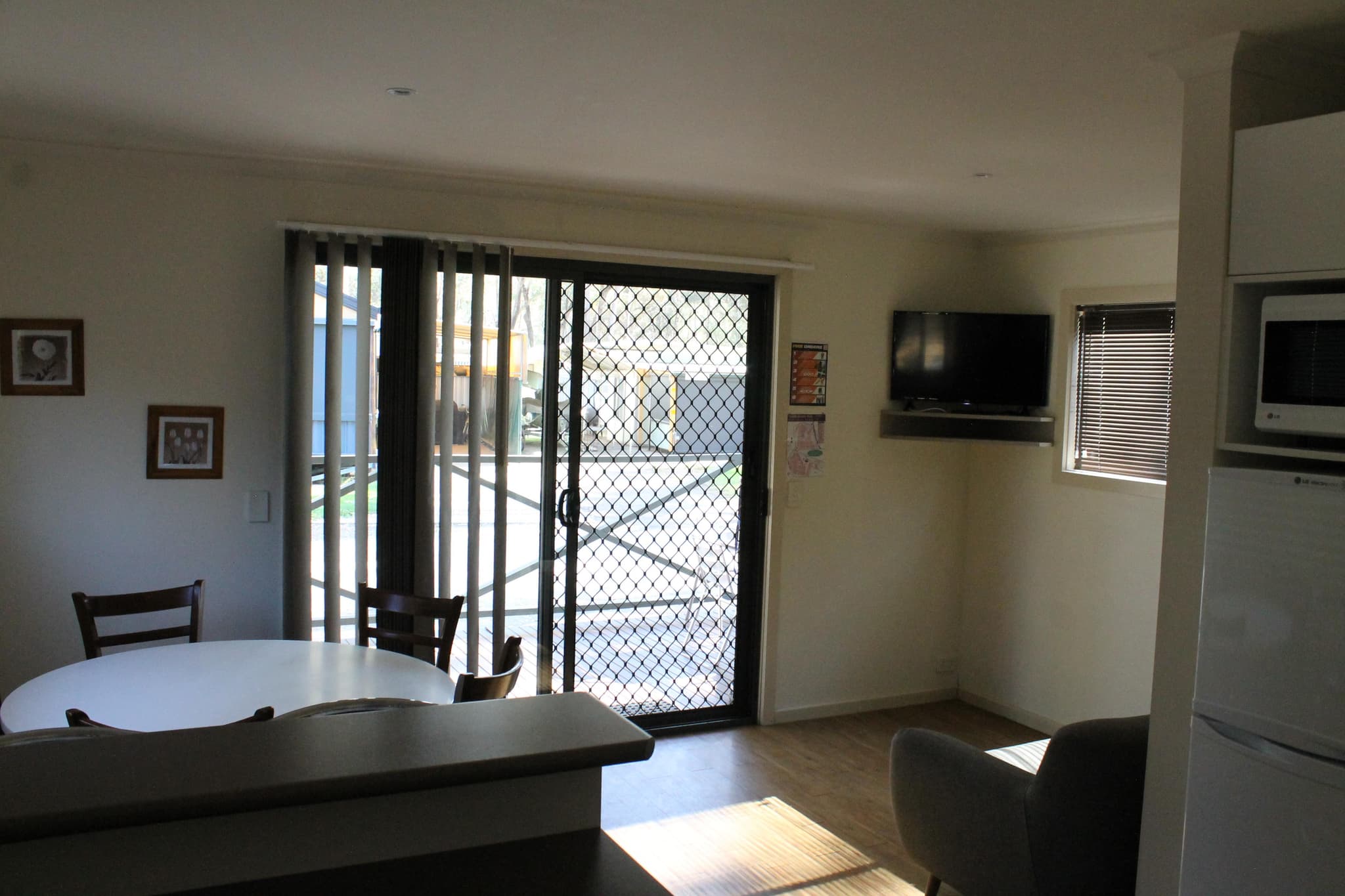 Living area of Southern Cross Cabin at Torrumbarry Weir Holiday Park, with wall-mounted TV, dining table and sliding door to deck