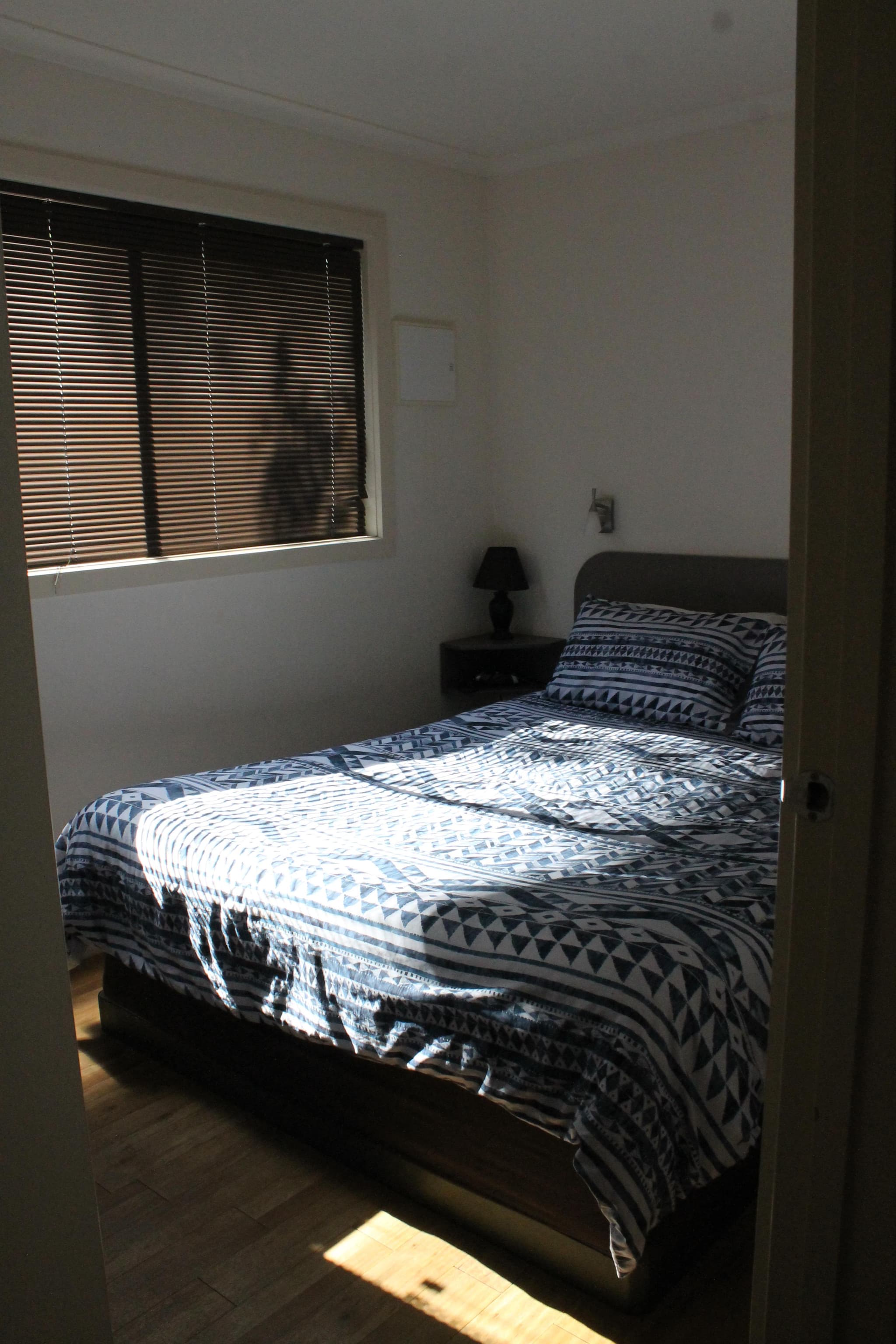 Bedroom in the Southern Cross Cabin at Torrumbarry Weir Holiday Park, queen bed with navy geometric quilt beside a timber bedside table and lamp