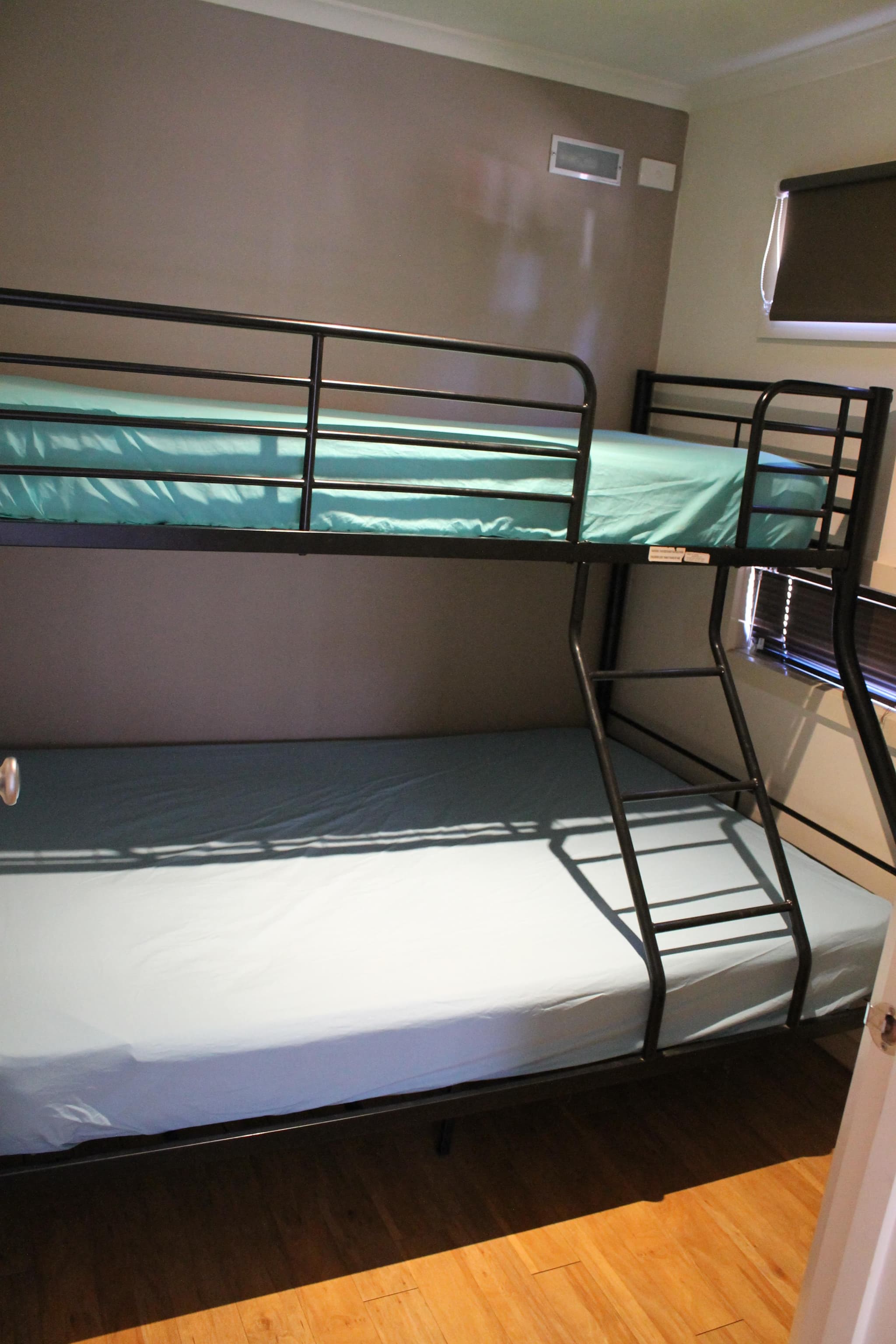 Black metal bunk bed with teal linen in a Southern Cross Cabin bedroom at Torrumbarry Weir Holiday Park, Patho VIC