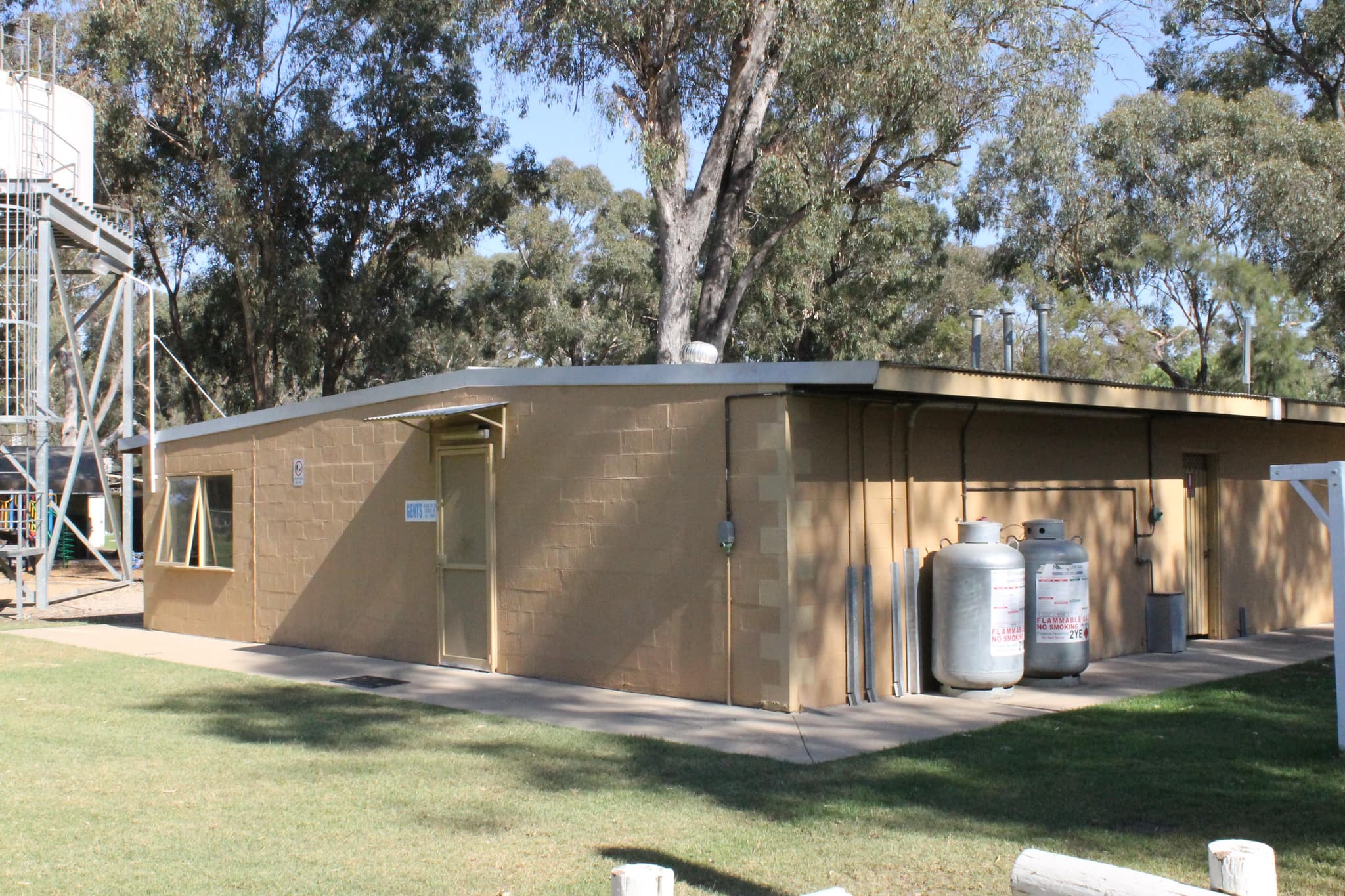 Amenities building at Torrumbarry Weir Holiday Park, Patho VIC, with gas cylinders and water tower amid shaded gum trees